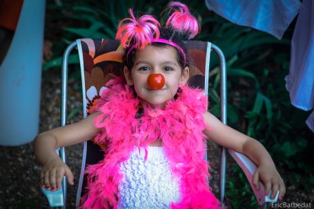 Fille souriante portant un costume de clown avec nez rouge et boa rose.