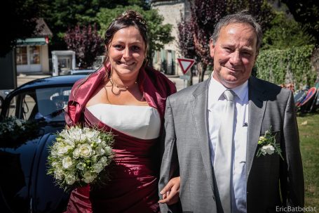 Une mariée souriante en robe blanche et rouge, marchant avec un homme en costume gris.