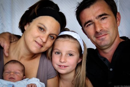 Famille souriante avec un bébé et deux enfants dans un cadre chaleureux.
