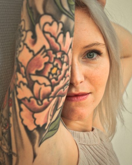 Femme avec un tatouage coloré de pivoine sur le bras, regardant vers l'objectif.