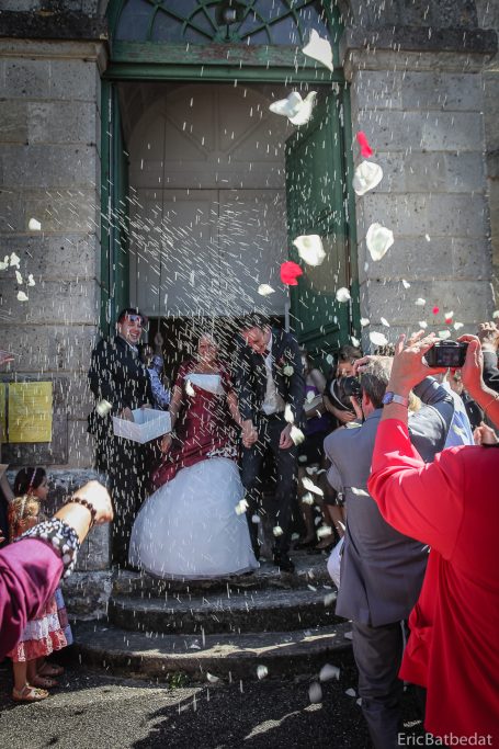 Mariés entourés d'invités, recevant des pétales de roses après la cérémonie.