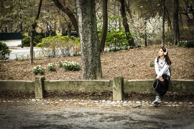 Fille assise sur un banc en plein air, entourée d'arbres et de feuilles mortes.
