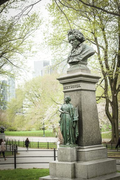 Statue de Beethoven avec un piédestal dans un parc, entourée d'arbres feuillus.