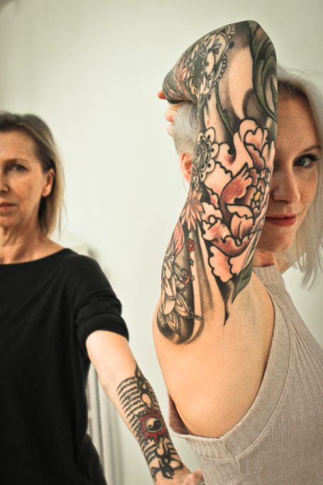 Deux femmes montrant des bras ornés de tatouages distincts.