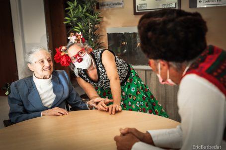 Deux personnes interagissent joyeusement avec une personne âgée autour d'une table.