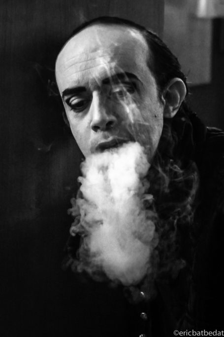 Homme en noir et blanc, fumant avec de la fumée s'échappant de sa bouche.