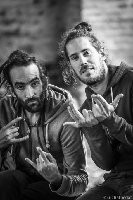 Deux hommes faisant des signes avec les mains, vêtus de sweats à capuche, en noir et blanc.