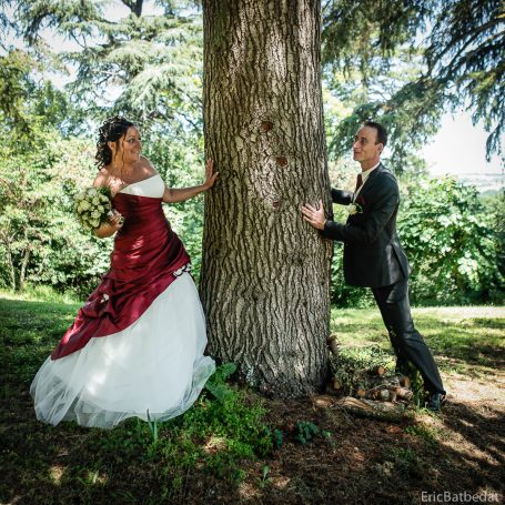 Une mariée en robe rouge et blanche pose près d'un arbre avec un homme en costume.