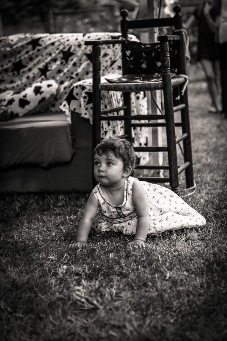 Bébé assis sur le sol près d'une chaise, entouré d'un décor naturel.