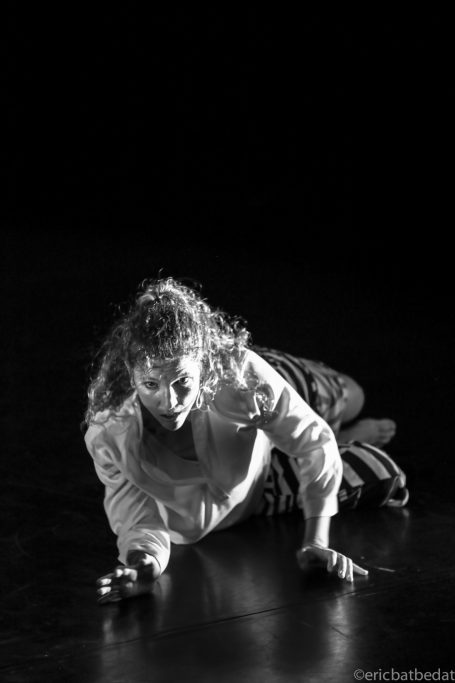 Une danseuse au sol, exprimant une intense émotion dans un éclairage sombre.