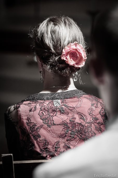 Femme de dos avec une rose dans les cheveux, vêtue d'une blouse en dentelle.