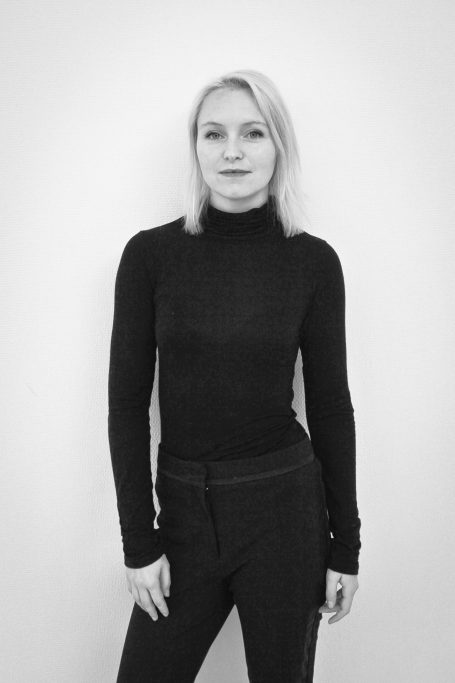 Femme en noir avec un haut à manches longues, regard neutre, pose debout.