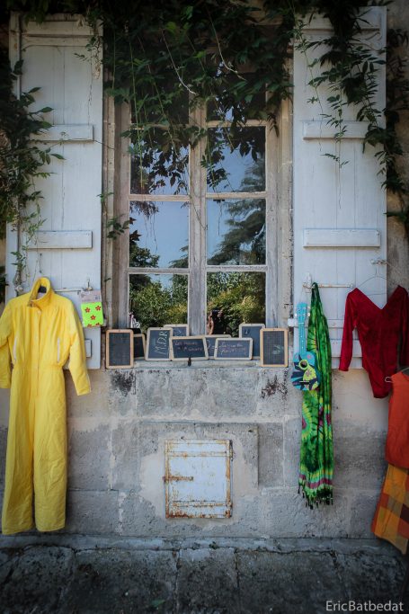 Vêtements colorés accrochés à un mur près d'une fenêtre encadrée de verdure.