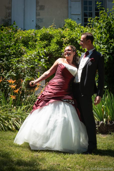 Une mariée en robe rouge et blanche pose avec un homme dans un jardin fleuri.