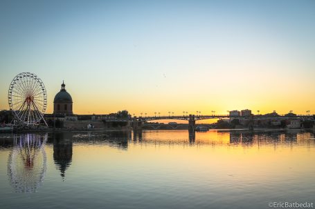 Vue au coucher de soleil d'une roue de Ferris et d'un dôme au bord d'une rivière.