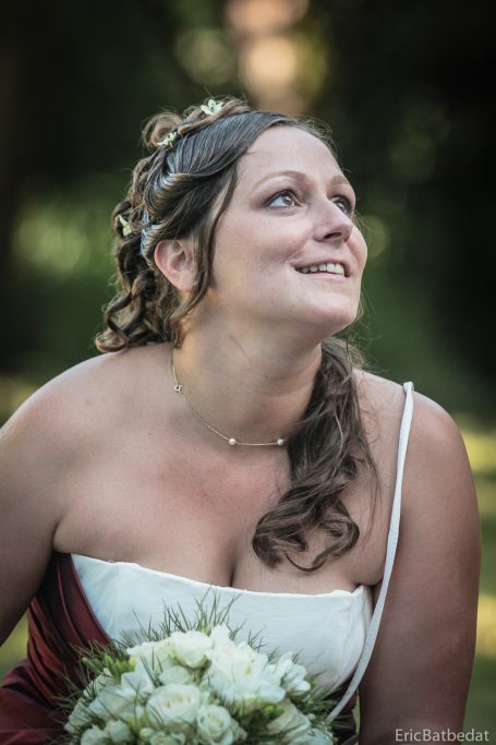 Femme souriante en robe de mariée tenant un bouquet de fleurs, regardant vers le ciel.
