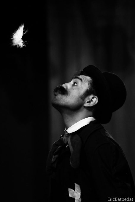 Un clown en costume avec moustache, regardant une plume blanche en vol.