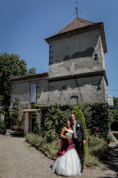 Une mariée en robe blanche et un homme en costume se tiennent devant un bâtiment en pierre.