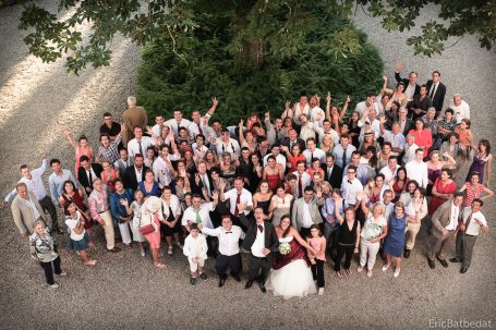 Groupe large de personnes célébrant un mariage en plein air, avec des sourires et des gestes de joie.