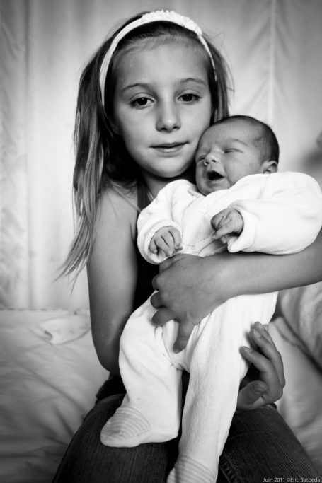 Une fille tient un bébé, tous deux souriant, en noir et blanc.