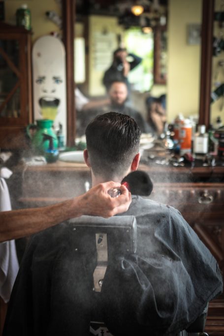 Un homme assis chez le coiffeur, recevant une coupe de cheveux, avec des produits autour.