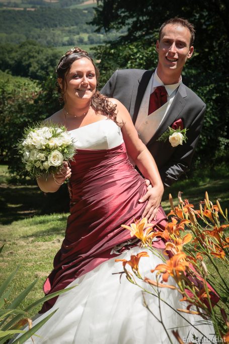 Mariage en plein air, couple souriant avec un bouquet, arrière-plan verdoyant.