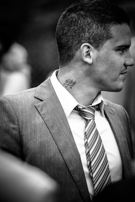 Homme en costume avec un tatouage sur le cou, regardant sur le côté.