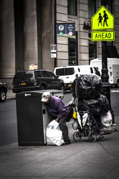 Une personne fouille une benne à ordures près d'un panneau de circulation.