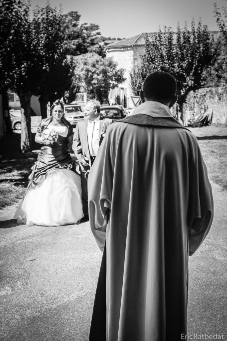 Un homme en manteau observe un groupe de mariés dans un parc.