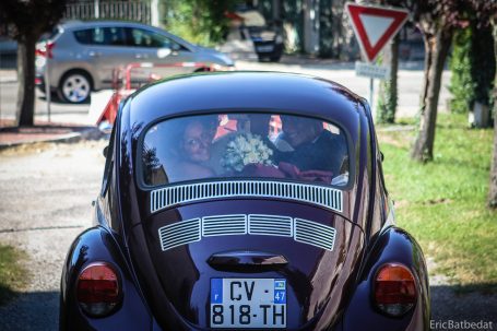 Voiture ancienne de couleur pourpre, avec des décorations de mariage à l'arrière.