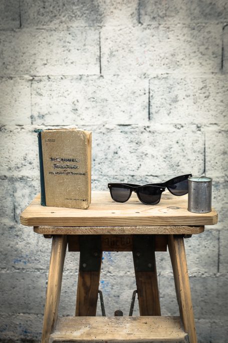 Livre ouvert, lunettes de soleil, et une boîte sur une petite table en bois.